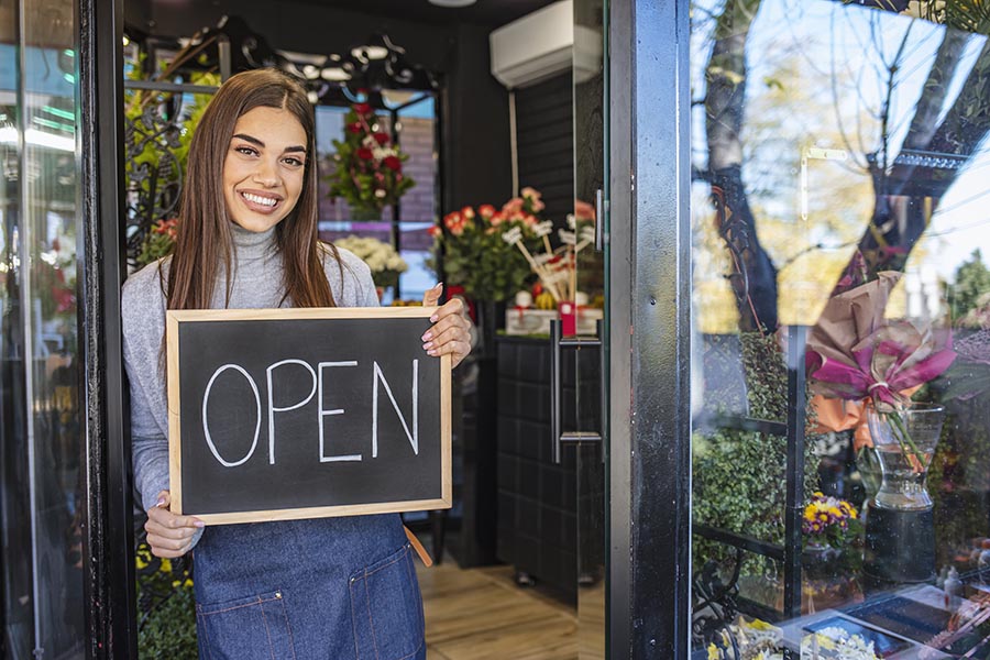 Business Insurance - Young Business Owner Holding a Chalkboard Sign Reading "Open" at the Door to Her Flower Shop