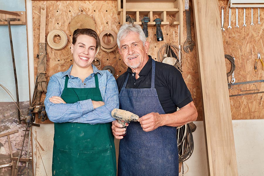 Specialized Business Insurance - Father and Daughter Contractors in a Wood Shop, Wearing Aprons and Standing in Front of Tools